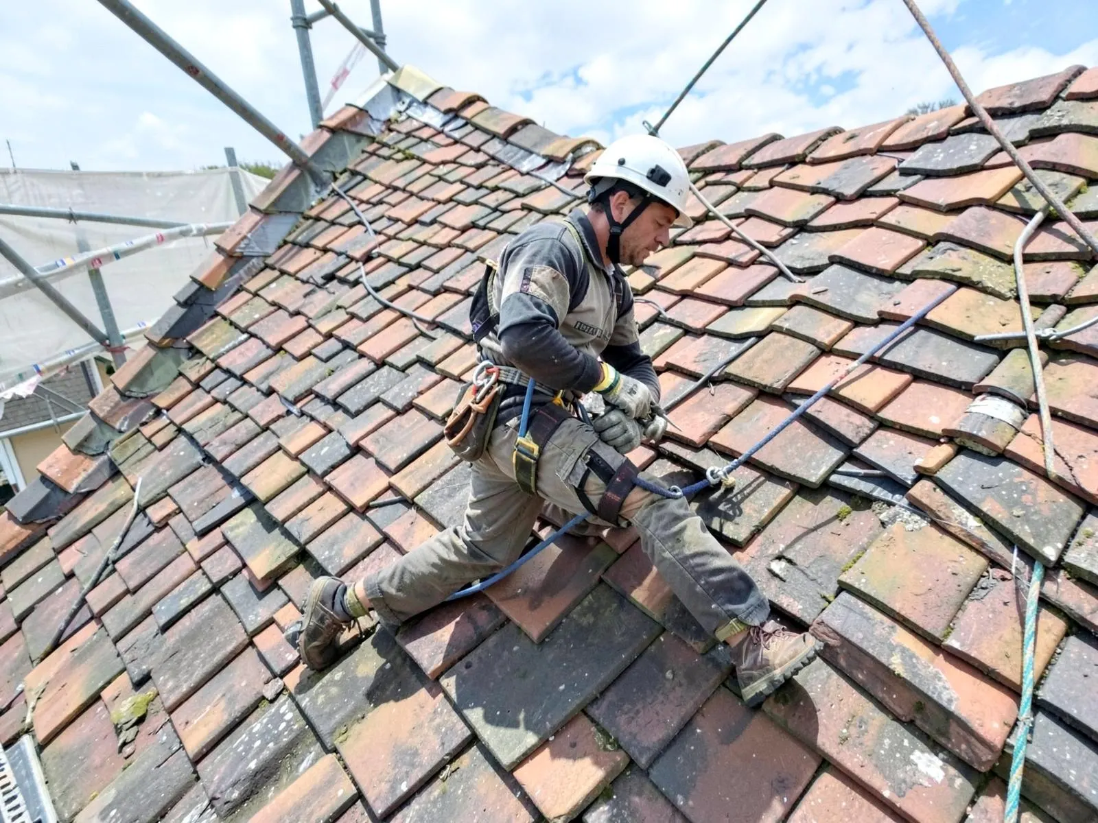 Dachdecker arbeitet angeseilt und mit Helm auf einem Steildach